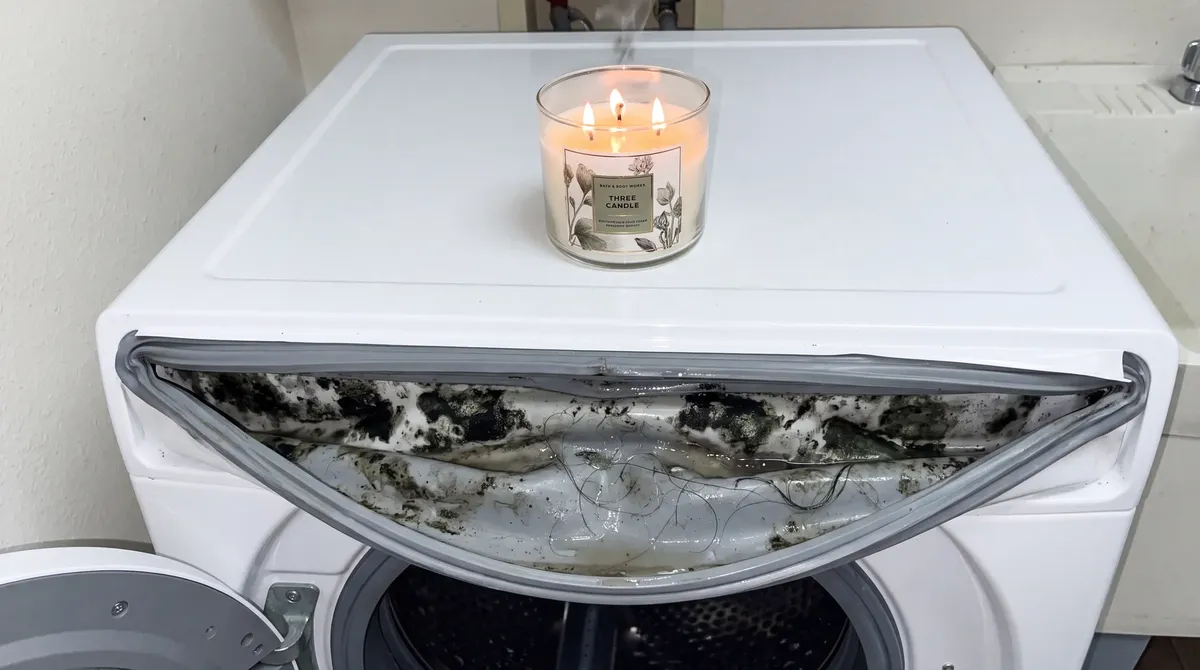 A scented candle on top of a washer whose drum is caked in grime